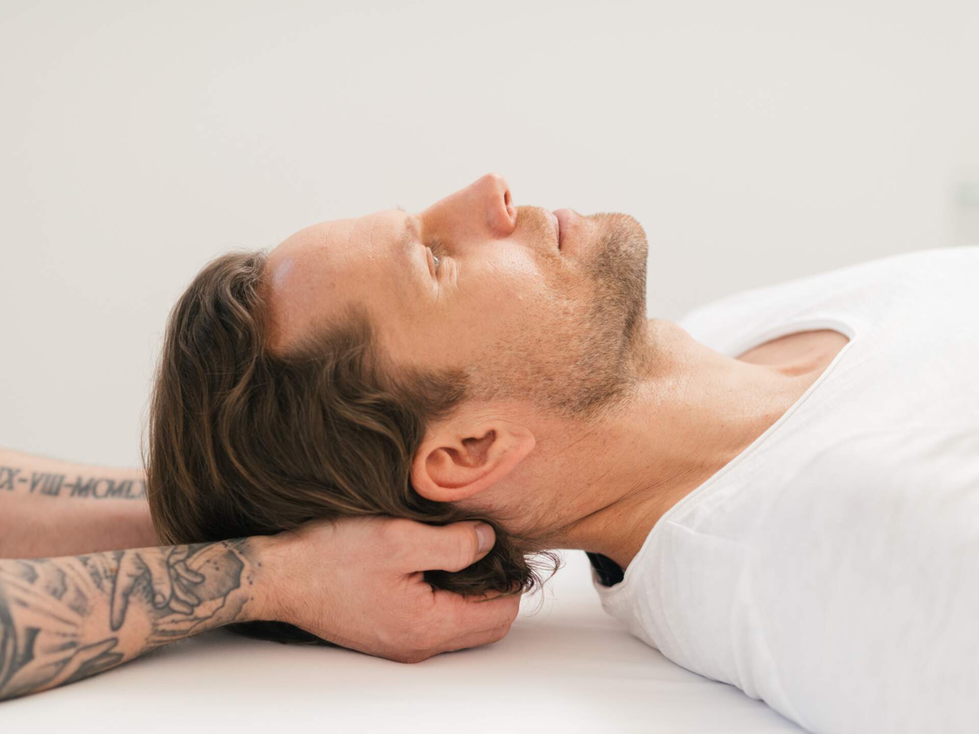 Man receiving neck massage, lying relaxed on white couch