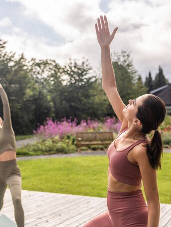Two women doing yoga in the park, one hand raised