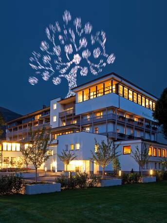 An illuminated hotel building glows at night beneath a radiant digital tree